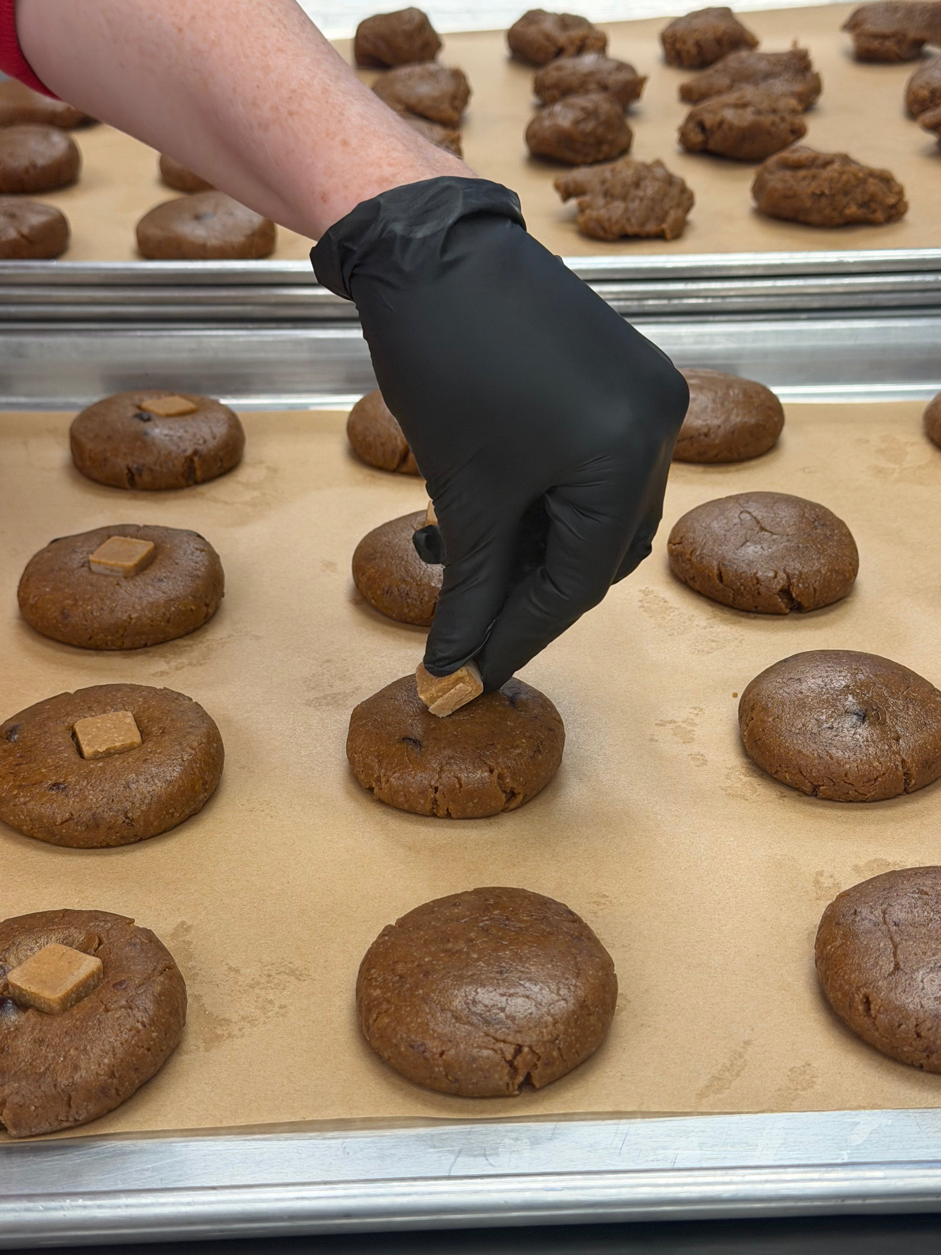 Hand wearing a glove placing peanut butter chips on top of peanut butter chocolate chip cookie