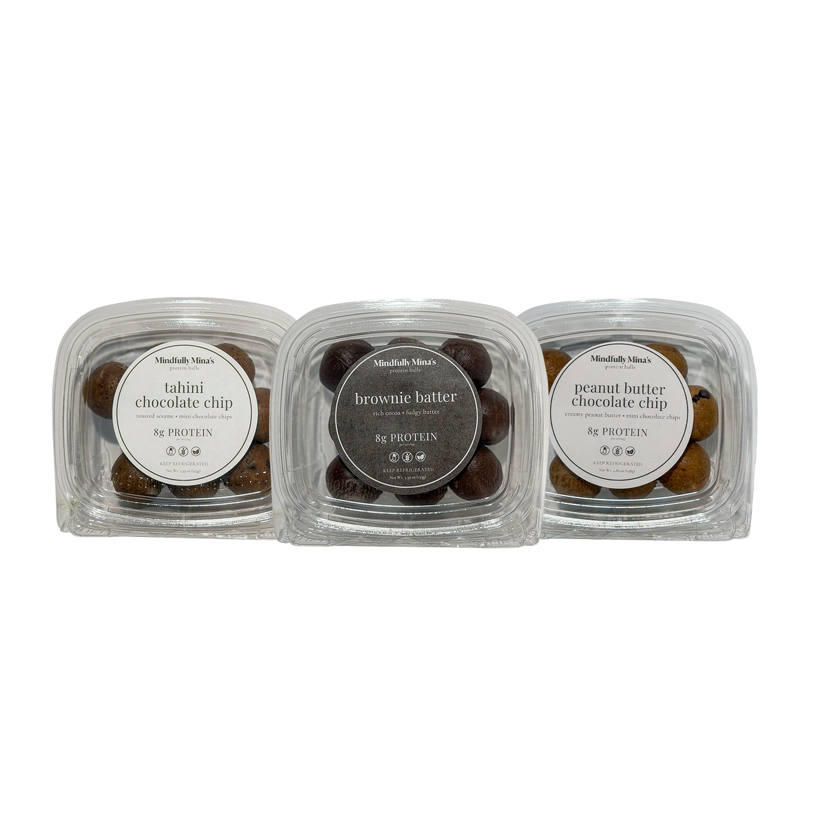 Three clear plastic containers of protein balls in a row, each with a round front label reading “8g protein”: tahini chocolate chip on the left, brownie batter in the middle, and peanut butter chocolate chip on the right. The balls are visible through the clear lids.