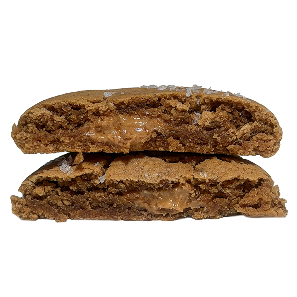 A cookie cut in half and stacked, showing a soft brown interior with a melty peanut butter center and flakes of sea salt on the crust.