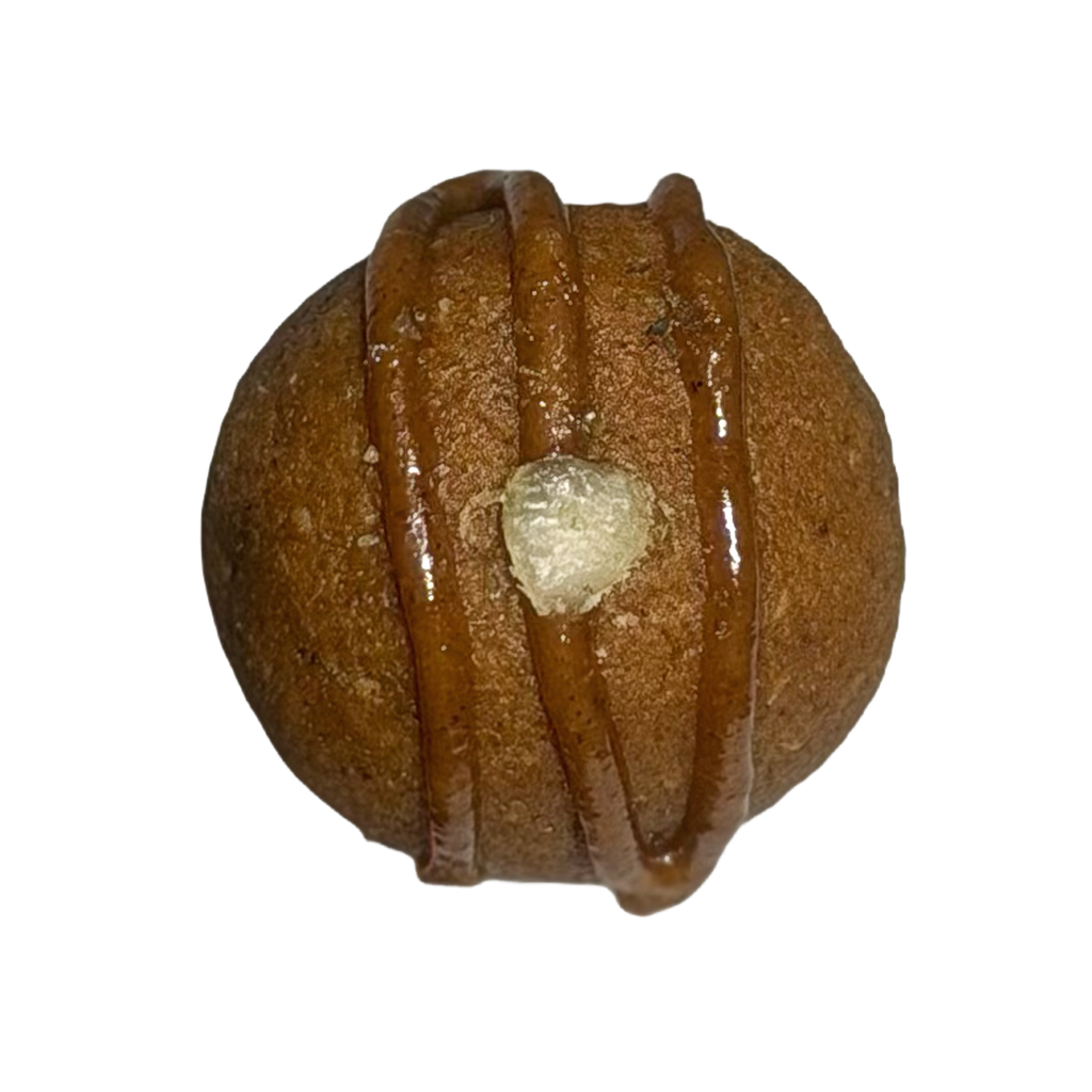 Top-down close-up of a single round pumpkin pie protein ball with three parallel lines of caramel-colored glaze and one pale pumpkin seed in the center.