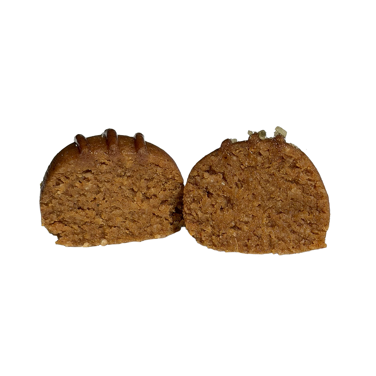 A pumpkin pie protein ball cut in half, showing a soft, dense, golden-brown interior. Thin glaze lines run across the top of one half, and crushed pumpkin seeds of topping sit on the other.